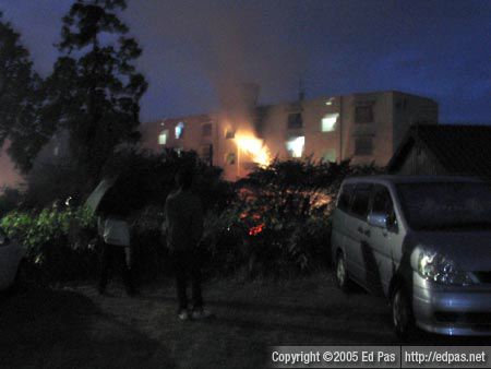 view of the burning building, from a parking lot up the hilll