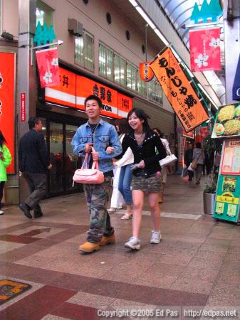 a young camo-wearing couple walking through the intersection in front of Crown Milan bakery in the Kokura arcades