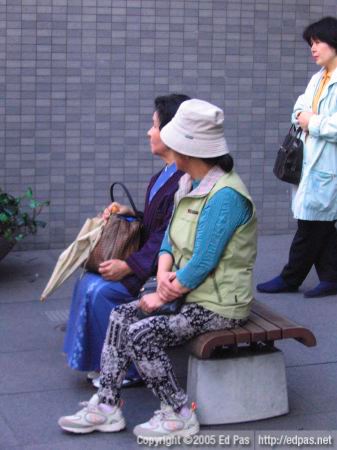 a couple of ladies sitting at the bus stop in front of Fukuoka Bank