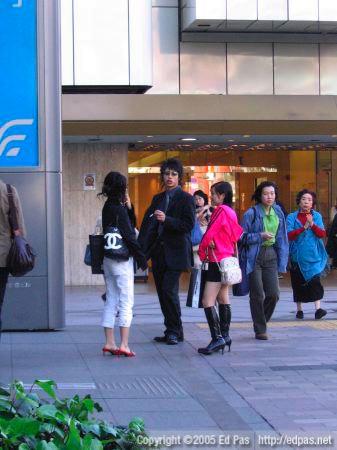 a young trio standing near the bus stop, with Izutsuya in the background