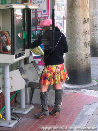 woman in eclectic clothing, using a phone book in front of Lawson in Kokura