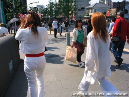 a couple in white, the woman on the left is shielding her face from the sun with her handbag