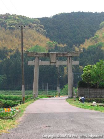 photo of the main torii of Nishi Ono Hachimangu, with farming lady starting a fire in the field in front of it