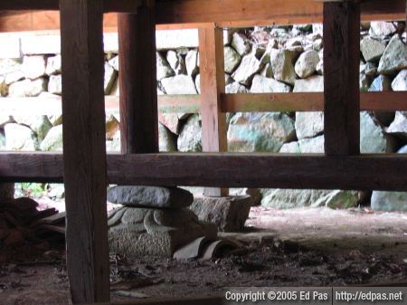 a view under the second shrine building, showing support beams and assorted foundation stones